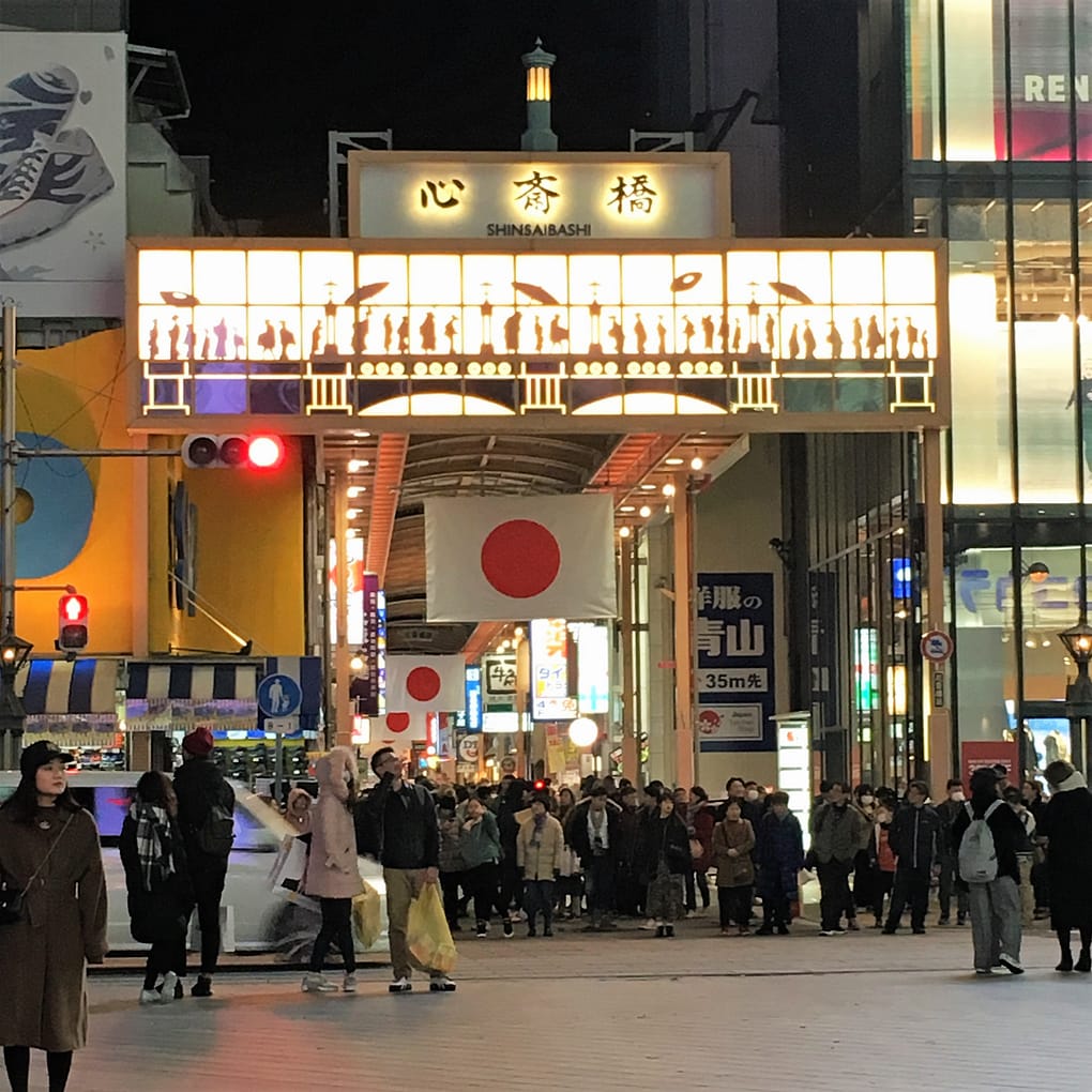 Shinsaibashi shopping area. Japanese flags hang from the ceiling of the covered shopping area. The area is crowded with people