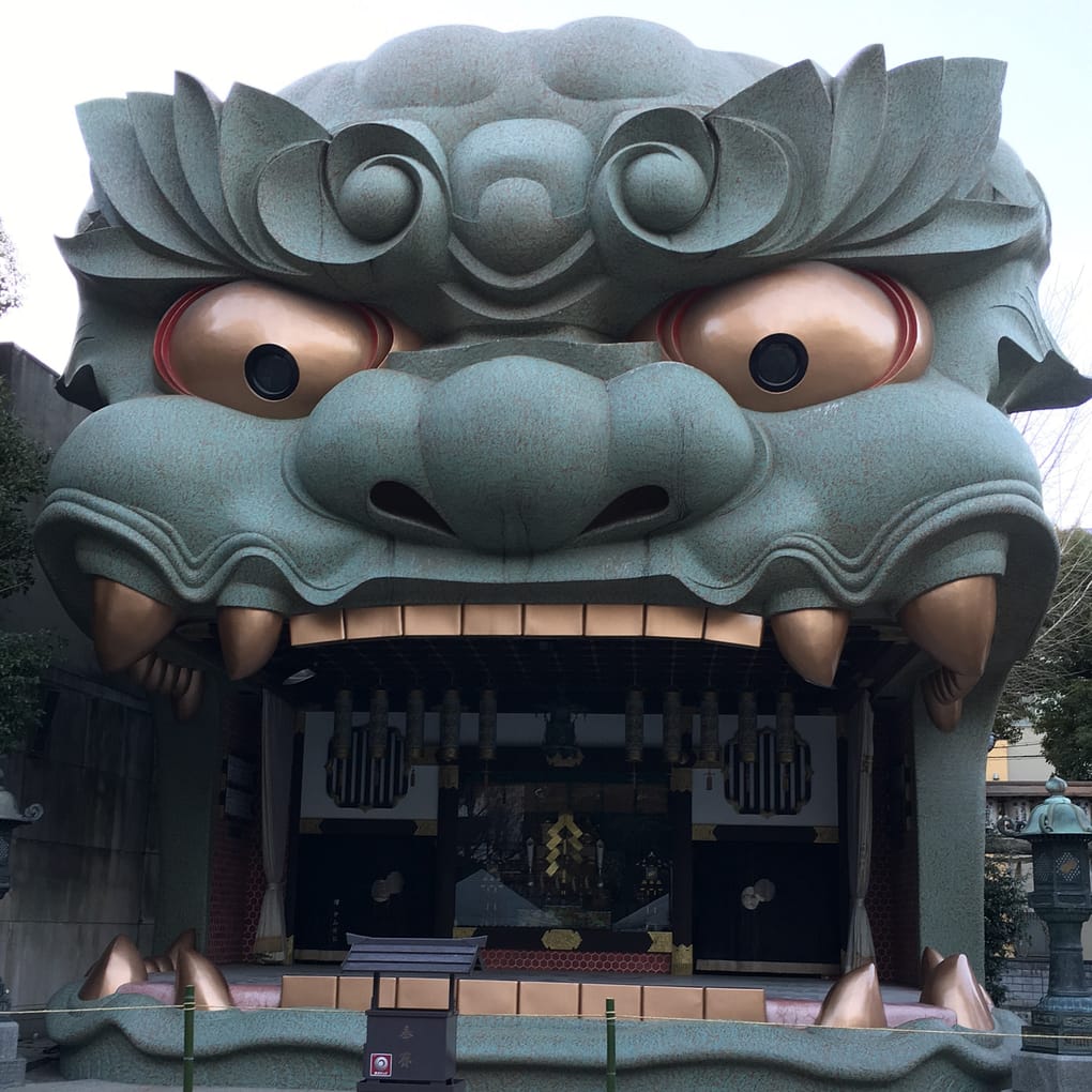 A close up of the lion head stage at Nambayasaka. The stage is green, with gold eyes and teeth. The mouth is open and holds the stage. The eyes, which function as lights, are pointed slightly downward