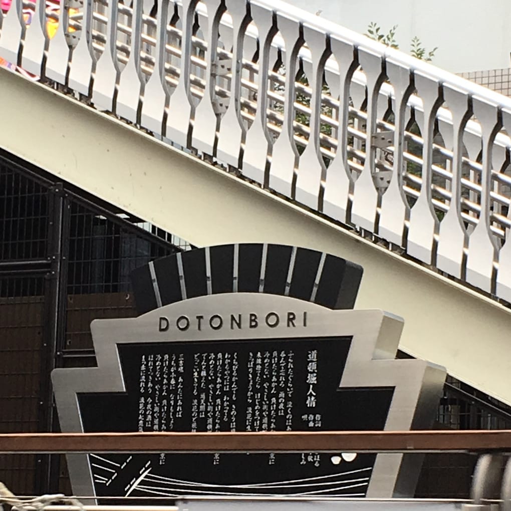 A sign in Japanese talks about the Dotonbori bridges. It is in front of the spatula bridge, which is constructed of spatula shapes alternating.