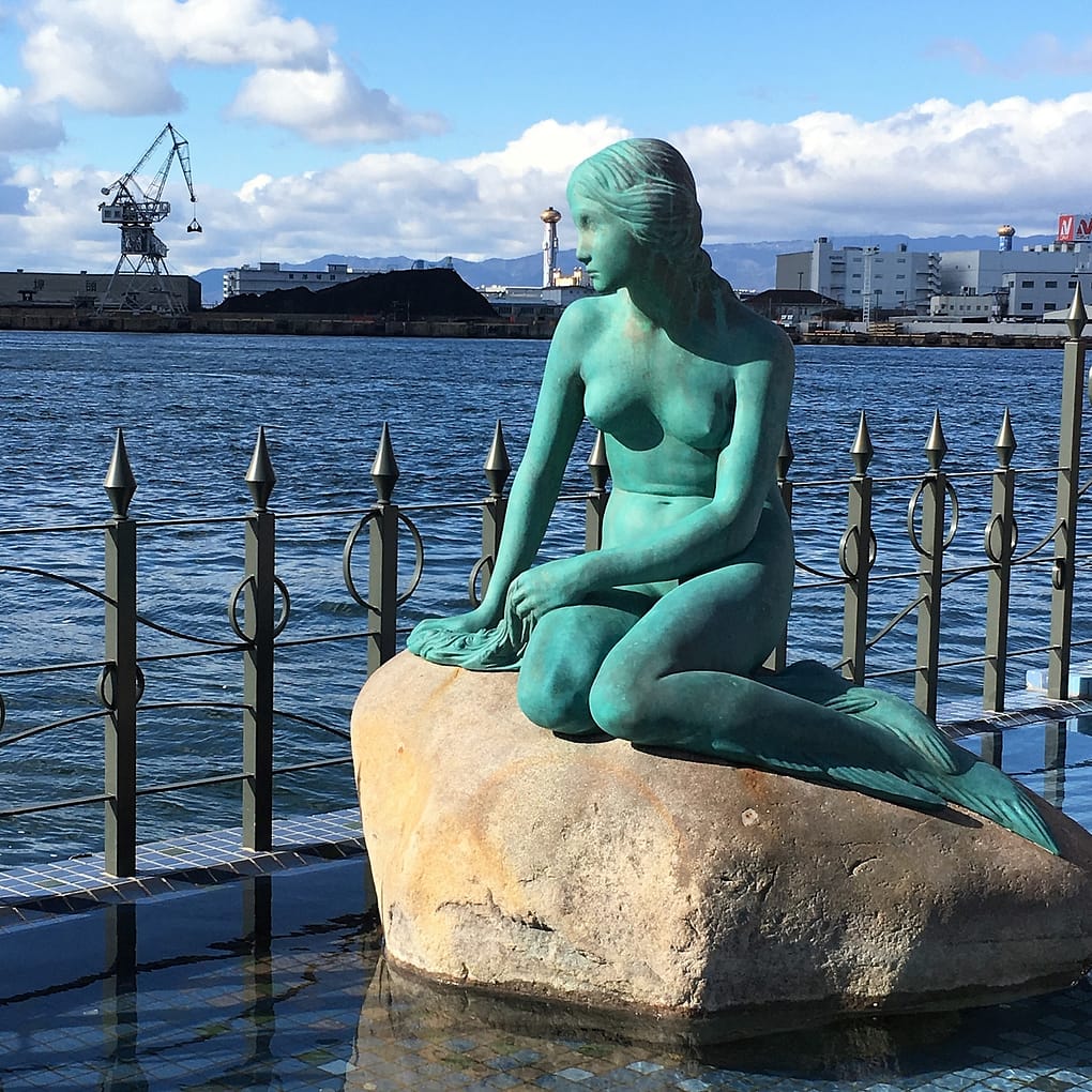 A green mermaid statue overlooks the Osaka bay area. The status is on a rock