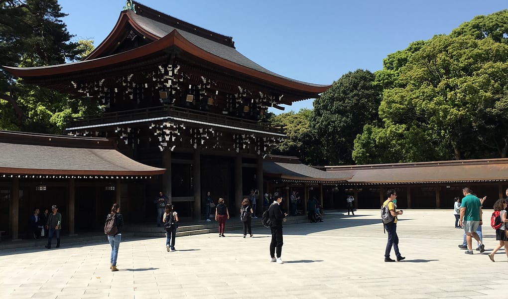 A dark wooden gate is stark against a cloudless blue sky and bright white courtyard tile.