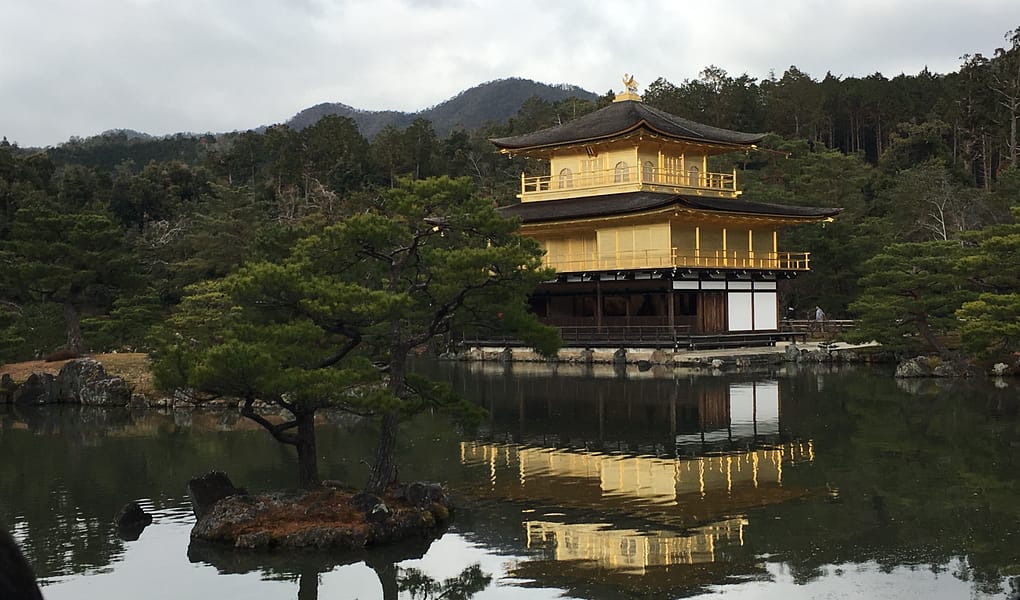 Kinkaku-ji, a temple covered in gold leaf, sits on the banks of a pond. The image of the temple is reflected in the pond's still waters
