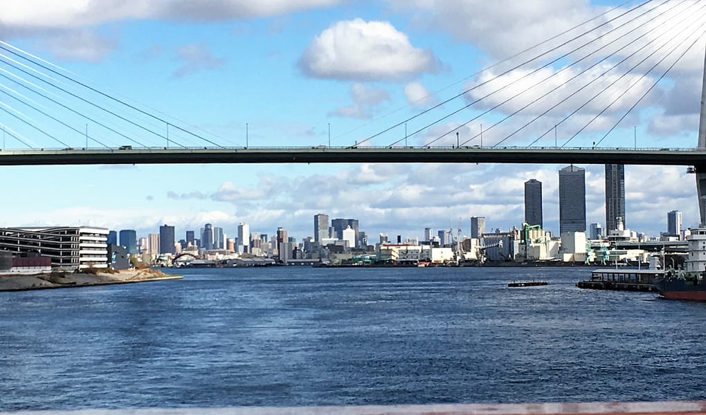 A view of the Osaka skyline from the Osaka bay. City buildings are in the background with water in the foreground.