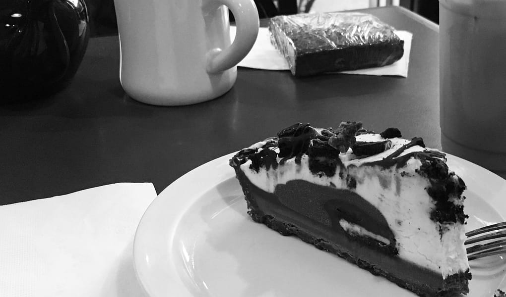 A black and white photo of coffee and a slice of oreo cheese cake.