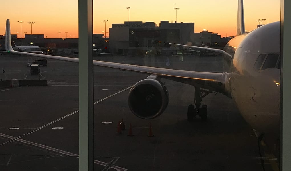A sunset through a window of an airport. A plane is parked in the foreground