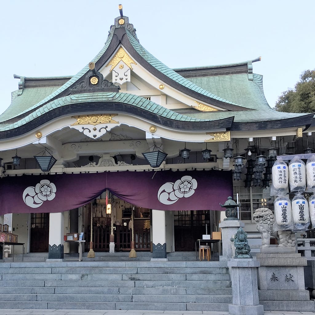 Shrine building decorated for the new year. Paper lanterns flank the sides of the building, which is green, white and gold.