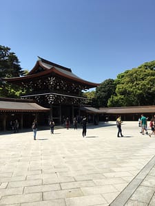 A dark wooden gate is stark against a cloudless blue sky and bright white courtyard tile.