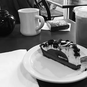 A black and white photo of coffee and a slice of oreo cheese cake.