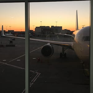 A sunset through a window of an airport. A plane is parked in the foreground