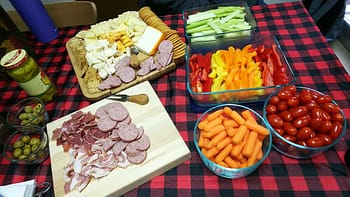 Two trays of charcuterie sit on a table with vegetables