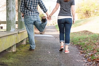 A man and woman hold hands while walking away from the camera. Only their shoulders and below is in the frame.