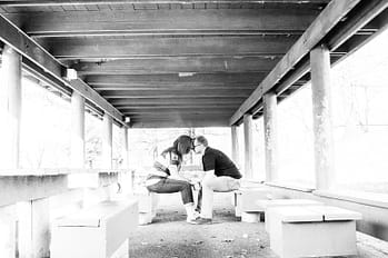 A black and white photo of a couple sitting with heads touching and holding hands.