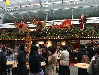 People stand in front of a wooden stall. The roof of the stall is decorated with garland and reindeer.