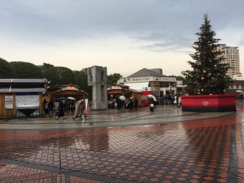 Three small wooden huts with a Christmas tree on the right.