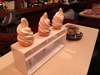 Three ice cream cones and a cup of coffee sit on a cafe table