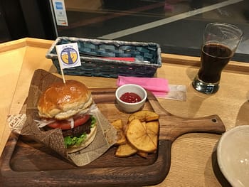 A small hamburger on a wooden cutting board sits next to a stout beer