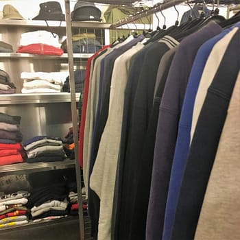 Cannonball thrift store sells new and used clothing. On the right of the frame are earth tone jackets. At the back are shelves of folded clothing.
