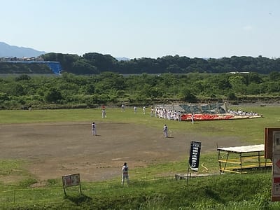 Image shows a grassy field with mountains in the background. The middle ground shows a large flat kite laying on the ground with people lined up at the top and bottom of the kite