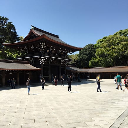 A dark wooden gate is stark against a cloudless blue sky and bright white courtyard tile.