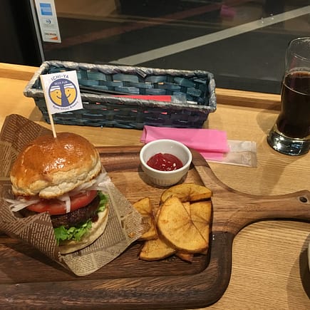 A small hamburger on a wooden cutting board sits next to a stout beer