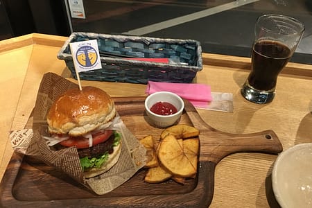 A small hamburger on a wooden cutting board sits next to a stout beer