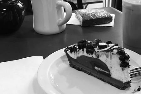 A black and white photo of coffee and a slice of oreo cheese cake.
