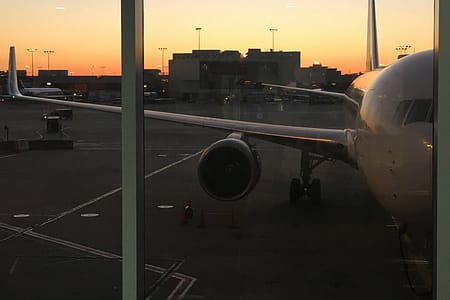 A sunset through a window of an airport. A plane is parked in the foreground