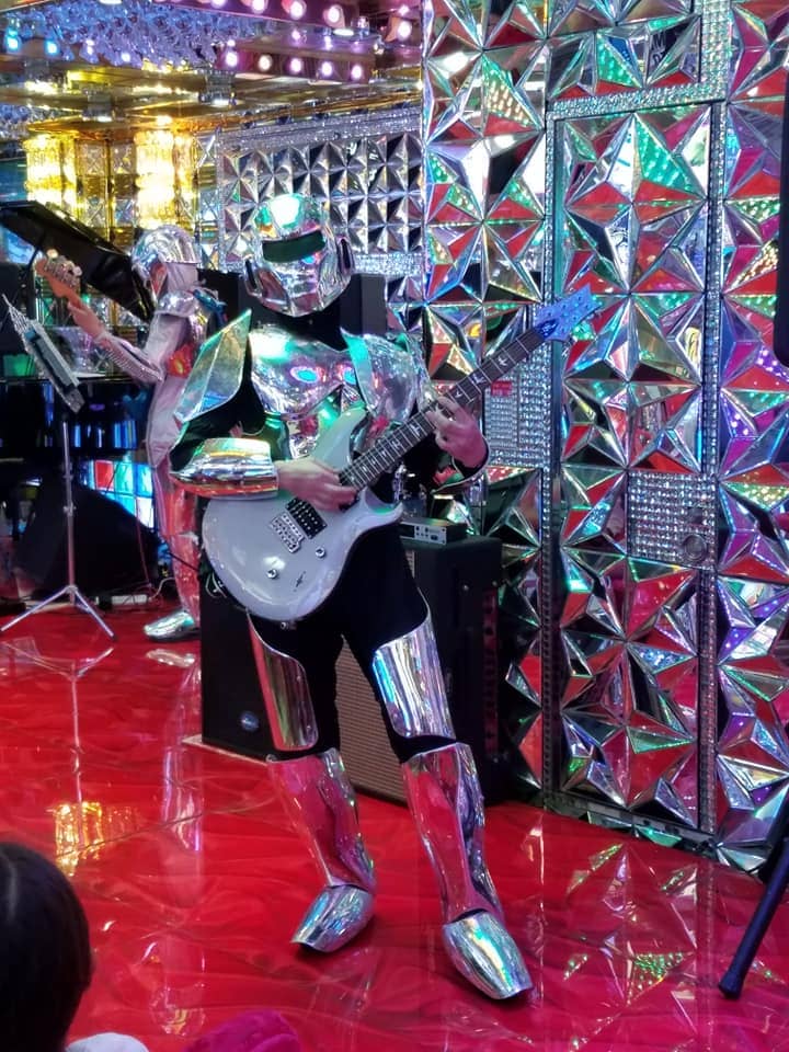 A performer dressed in a shiny robot costume in front of a mirror wall