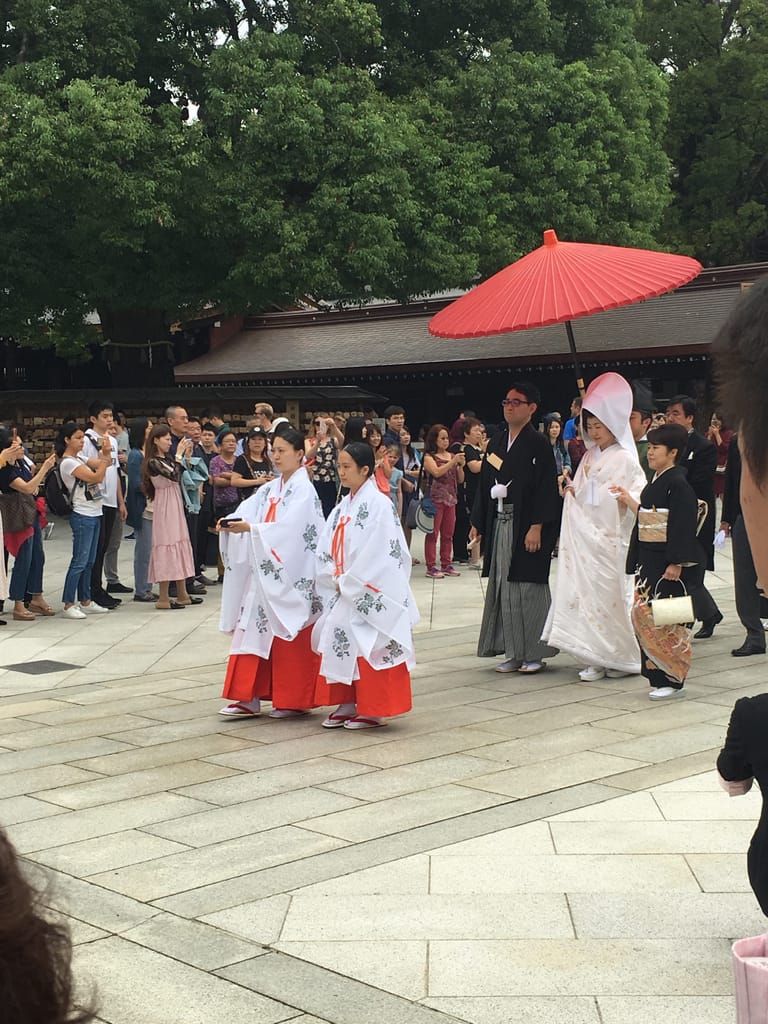 A bride is escorted through the courtyard. Two attendants are in front, the groom beside her.