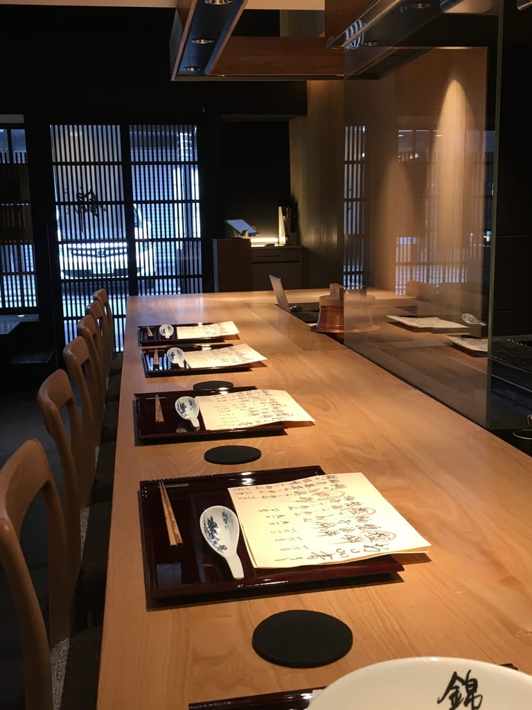 Bar seating at Ramen Nishiki. Each place setting has a wooden tray, a menu, a spoon and wooden chopsticks