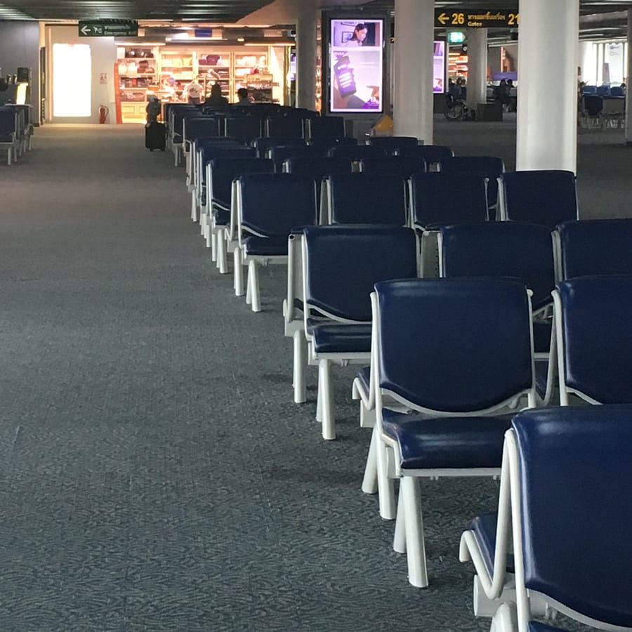 An empty airport terminal in Asia. Seats line up in the frame diagonally, starting from the lower right corner